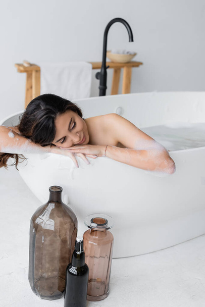 Mujer joven en espuma relajante mientras toma baño en baño moderno  - Foto, imagen