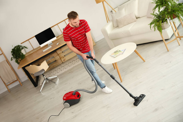 Young man using vacuum cleaner at home - Valokuva, kuva