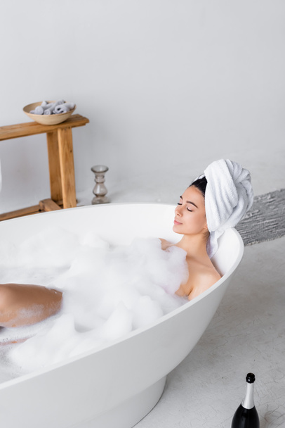 Woman taking bath with foam near bottle of champagne  - Photo, Image