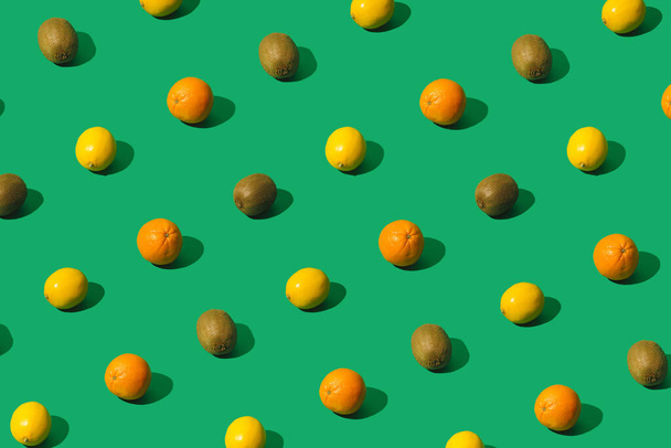 Lemons, oranges and kiwis creative pattern on a green background. Minimal sunlit layout. - Photo, Image