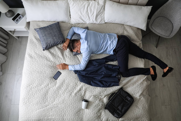 Виснажений бізнесмен в офісному одязі спить на ліжку вдома після роботи, вид зверху
 - Фото, зображення