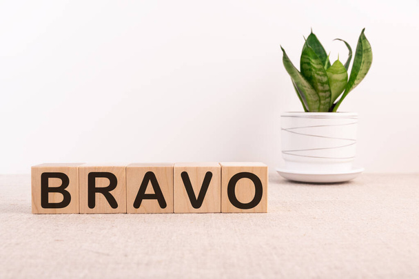 The word Bravo is written in cubes on a light table with a flower and a light background. - Foto, Imagem