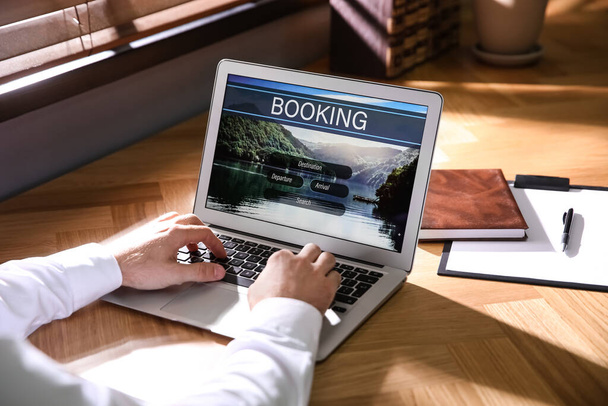 Man with laptop booking tickets online at wooden table, closeup. Travel agency concept - Photo, Image