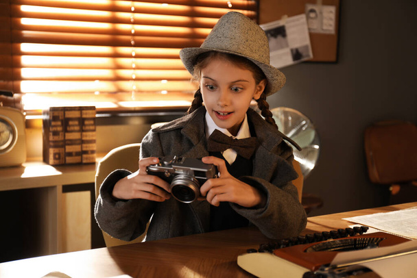 Cute little detective with camera at table in office - Foto, imagen