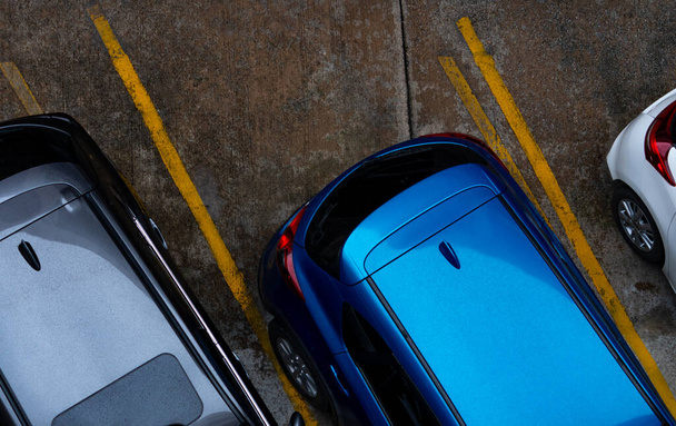 Blick von oben auf das auf einem Betonparkplatz geparkte Auto mit gelbem Verkehrszeichen auf der Straße. Obere Ansicht des Autos in einer Reihe auf dem Parkplatz. Kein freier Parkplatz. Außerhalb der Parkplätze.  - Foto, Bild