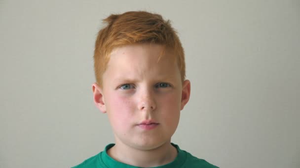 Portrait of serious red hair boy with freckles. Adorable handsome baby looking into camera indoor. Close up emotions of male child with sad expression on face. Slow motion - Footage, Video