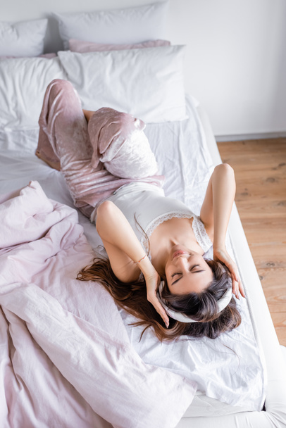 High angle view of woman in pajama and headphones lying on bed during morning - Φωτογραφία, εικόνα