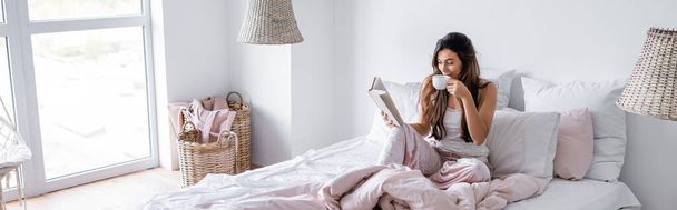 Nuori nainen kupin kahvia käsittelyssä kirja sängyllä, banneri  - Valokuva, kuva