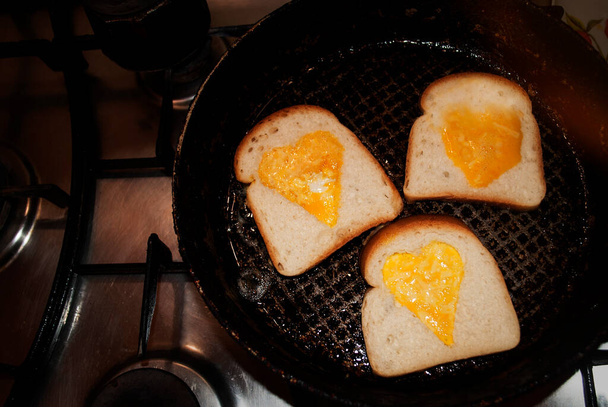 Egg, heart-shaped omelette in toasted slice of gluten-free bread fried in a pan. Valentine's day concept. Homemade creative food. Festive lunch or breakfast. The whip cooking process. - Photo, Image