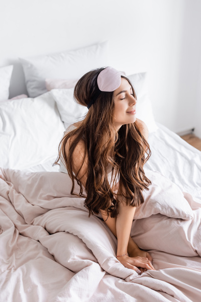 Brunette woman in blindfold sitting on bed at home  - Foto, Imagen