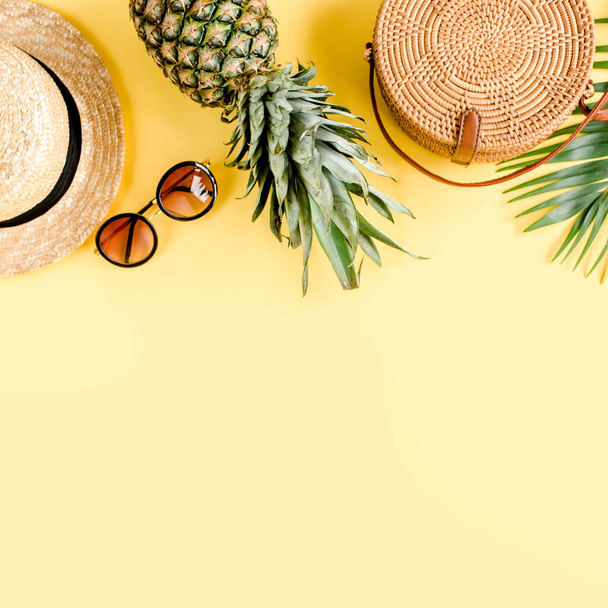 Womens accessories traveler: bamboo bag, straw hat, tropical palm leaves monstera, retro camera on yellow background. Flat lay, top view - Photo, Image