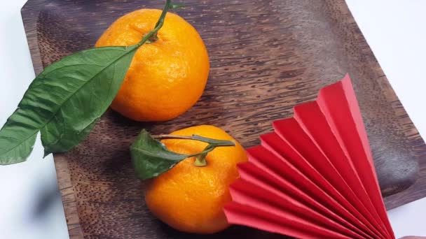 Una mano mette gli appassionati di carta origami rossi su un piatto di legno scuro di mandarini. Sfondo festivo Capodanno cinese, creatività video 4K - Filmati, video