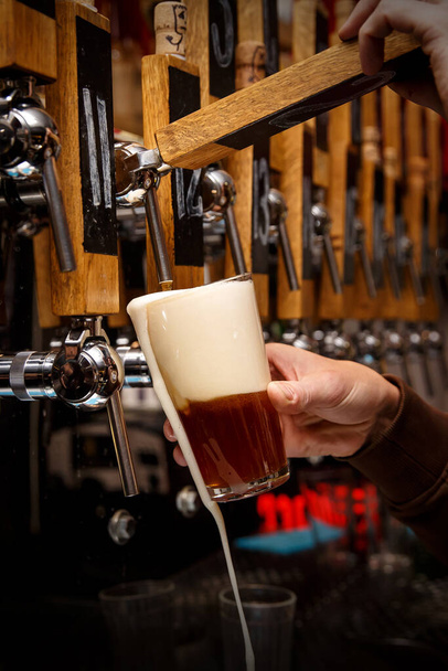 Le mani del barman versano una birra scura in un bicchiere. - Foto, immagini