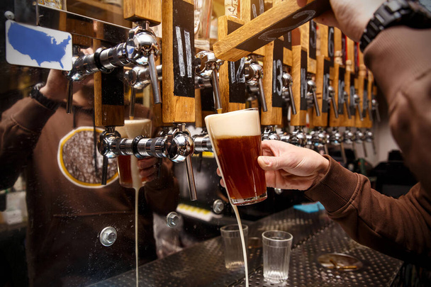 Baarimikko kaataa hanasta tuoretta olutta lasiin pubissa, baarissa - Valokuva, kuva