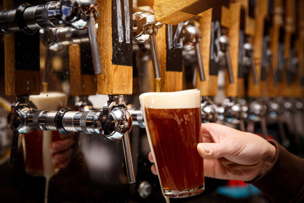Barkeeper gießt in Kneipe, Bar aus dem Zapfhahn frisches Bier ins Glas - Foto, Bild