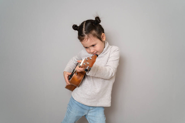 Маленька дівчинка грає укулеле. Творчий розвиток у дітей. Музична освіта з дитинства. Викладання музики онлайн вдома
 - Фото, зображення