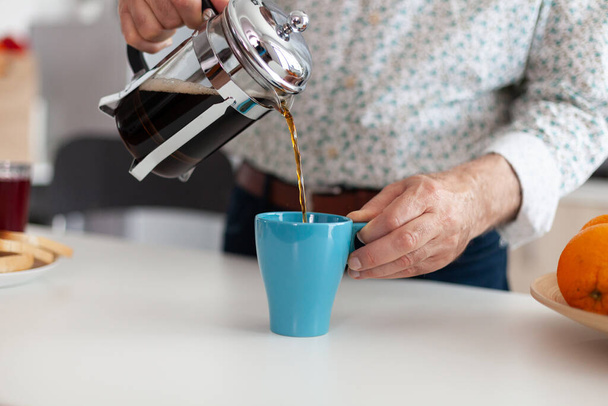 Rentner mit blauer Tasse auf Tisch gießt aromatisches Getränk aus Kaffeemaschine - Foto, Bild