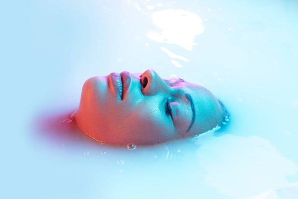 Beautiful female face in the milk bath with soft glowing in blue-pink neon light - Foto, Imagem