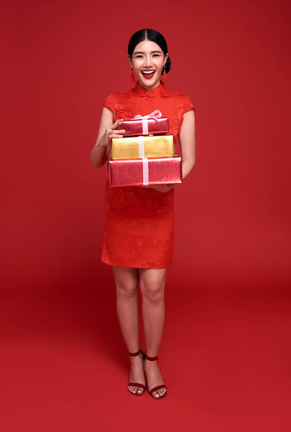 Happy Chinese new year. Asian woman wearing traditional cheongsam qipao dress holding gift box isolated on red background. - Photo, Image