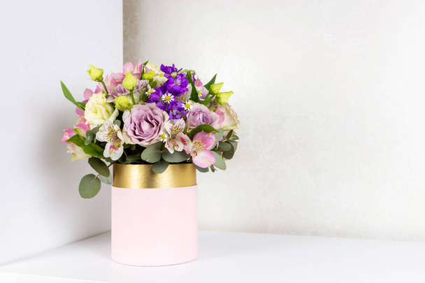 Mooi boeket bloemen in roze ronde doos op een witte tafel. Cadeau voor vakantie, verjaardag, bruiloft, moederdag, Valentijnsdag, Vrouwendag. Bloemen arrangement in een hoedendoos. - Foto, afbeelding