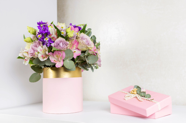 白いテーブルの上に丸い箱とピンクのギフトボックスの花の美しい花束。休日、誕生日、結婚式、母の日、バレンタインデー、女性の日のための贈り物。帽子箱の花の配置. - 写真・画像