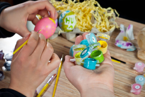 Mother and son paint Easter eggs. Multicolored Easter eggs on a wooden table background. Traditional family entertainment before the holiday. - Zdjęcie, obraz