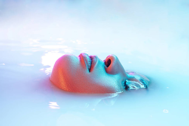 Beautiful female face in the milk bath with soft glowing in blue-pink neon light - Photo, Image