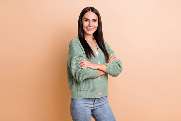 Portrait of optimistic girl crossed arms wear green sweater jeans isolated on peach color background - Foto, immagini