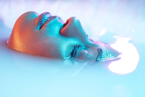 Beautiful female face in the milk bath with soft glowing in blue-pink neon light - Fotoğraf, Görsel