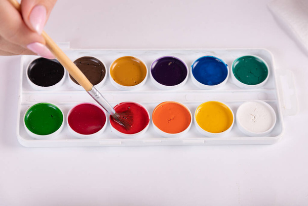 Set of watercolor paints, hand holds a brush for painting. - 写真・画像