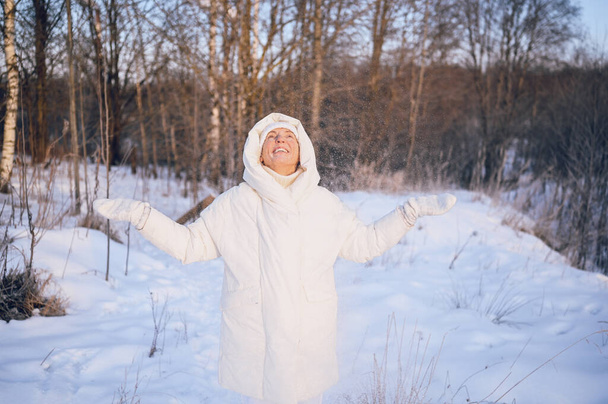 Heureuse femme mûre âgée en tenue chaude blanche jouant avec la neige en hiver ensoleillé à l'extérieur. Retraités en bonne santé vacances vacances activités d'hiver, concept de mode de vie actif - Photo, image