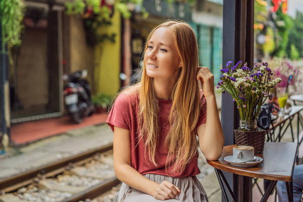 Young woman traveler drinks Vietnamese coffee with egg sitting by the railway paths which go through residential area in Hanoi city. Hanoi Train Street is a famous tourist destination. Vietnam reopens - Photo, Image