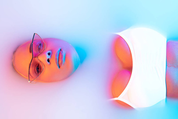 Beautiful female face in the milk bath with soft glowing in blue-pink neon light - Fotografie, Obrázek