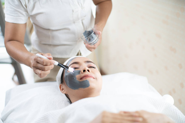 Gezicht huidverzorging. Een Aziatische vrouw maskeert haar gezicht in een spa salon. Vrouw met cosmetische spa gezichtsmasker. - Foto, afbeelding