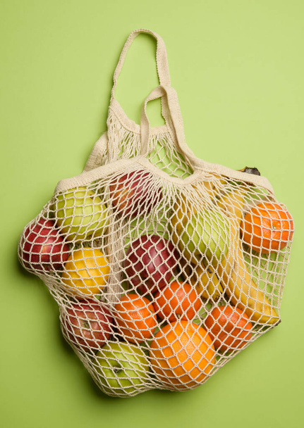 ripe fresh fruits in a textile string bag on a green background, top view - Фото, изображение