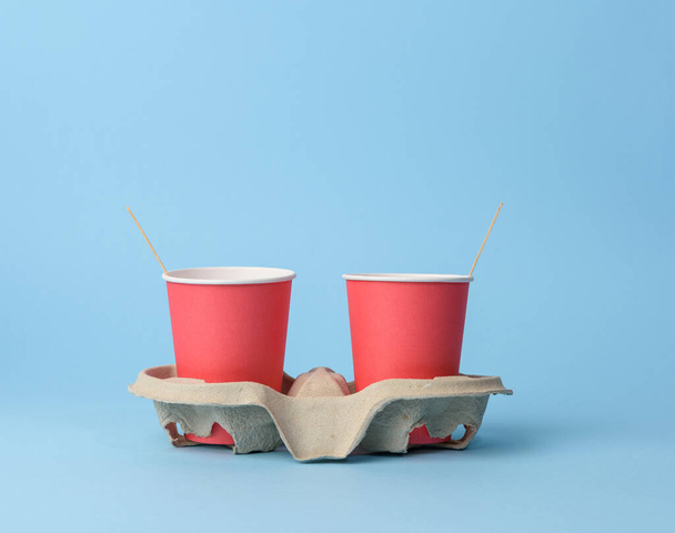 красные одноразовые стаканчики в держателе бумаги на синем фоне, отказ от пластика, ноль отходов - Фото, изображение