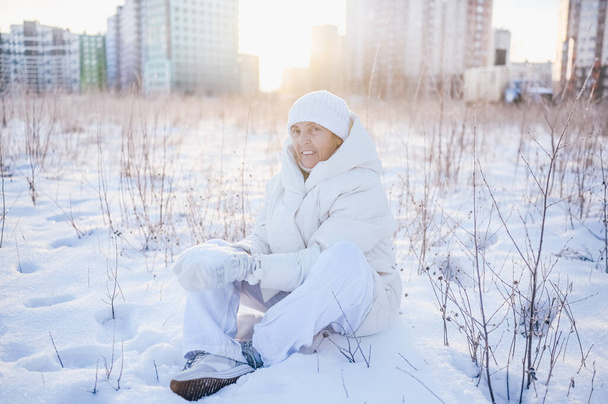 Happy elderly senior mature woman in white warm outwear playing with snow in sunny winter outdoors. Retired healthy people holiday vacation winter activities, active lifestyle concept - Foto, Imagem