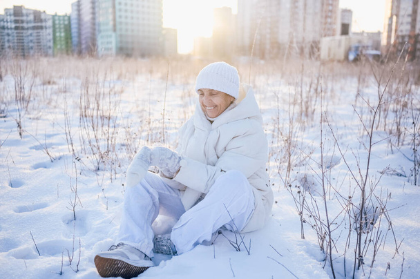 Happy elderly senior mature woman in white warm outwear playing with snow in sunny winter outdoors. Retired healthy people holiday vacation winter activities, active lifestyle concept - Photo, Image