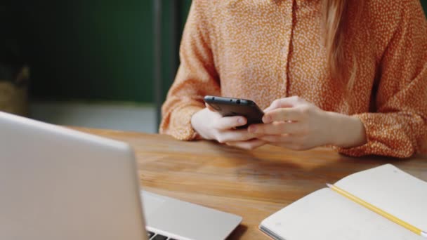 Środek kadru młodej bizneswoman siedzącej w biurze i przewijającej się przez media społecznościowe na smartfonie - Materiał filmowy, wideo