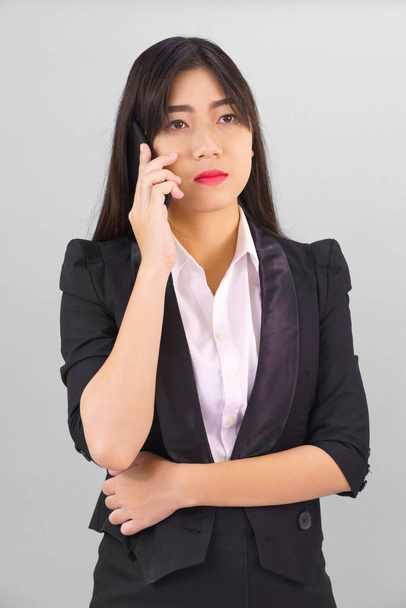 Young Asian women in suit standing posing using her phone against gray background - Фото, изображение