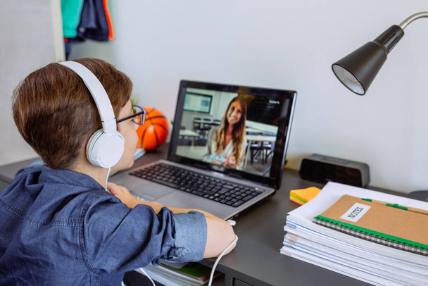 Jongen met hoofdtelefoon die thuis les krijgt met laptop uit zijn slaapkamer - Foto, afbeelding