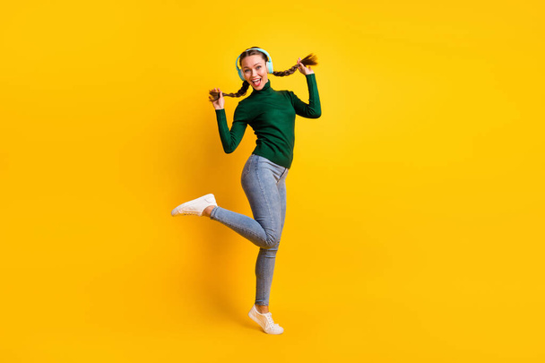 Full length body size view of pretty cheerful girl listening music jumping dancing isolated on bright yellow color background - Foto, afbeelding