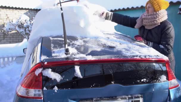 Kobieta czyszcząca śnieg z samochodu szczotką samochodową po ogromnej burzy śnieżnej - Materiał filmowy, wideo