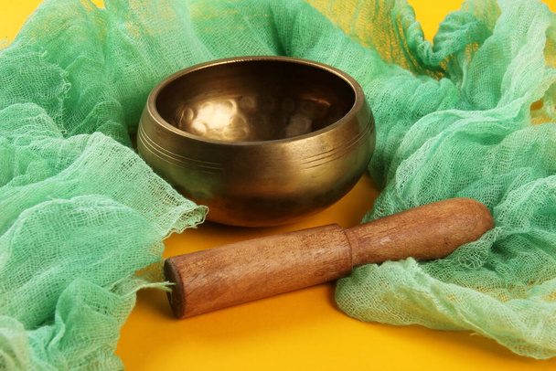 Тибетська чаша, що співає з дерев "яною палицею на жовтому фоні, зелена тканина. - Фото, зображення