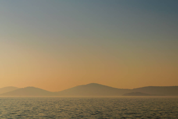 Hazy sunset seascape with sea horizon and clear sky, with mountain islands, natural photo background - Photo, Image