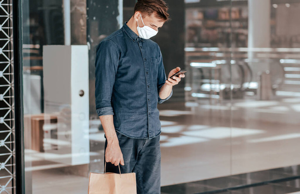 man with a shopping bag reading a message on his smartphone. - Foto, imagen