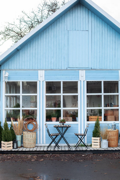 Exterieur blauw huis met een prachtig terras decoratie groene planten. Gezellig rustiek huis in het land. Voorgevel huis met rieten manden, houten tafel en stoelen op de veranda. Levende kerstboom in pot - Foto, afbeelding