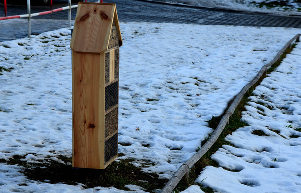 houses for insects, hotels for solitary bees, beetles attracting  and butterflies for moths and butterflies. in a city park on a housing estate in the winter stands in the snow, road barrier - Фото, изображение