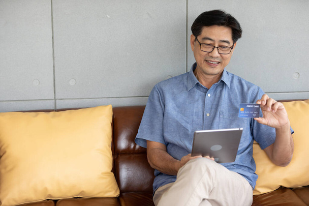 senior asiático hombre usando tablet para compras en línea y pagar con tarjeta de crédito - Foto, imagen