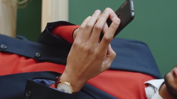 Close up tiro de empresário elegante em pé contra a parede verde e digitando no smartphone - Filmagem, Vídeo